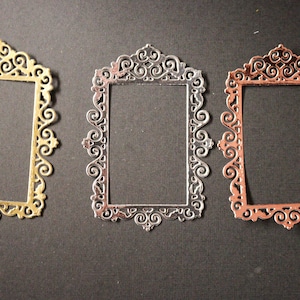 May include: Three ornate metal picture frames in gold, silver, and copper. The frames are all the same size and shape, with a delicate, scroll-like design.