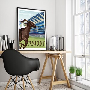 May include: A framed art print featuring a horse race scene at Ascot. The artwork depicts a brown horse with a jockey in green and white racing attire. The word "ASCOT" is displayed in large letters, with "SINCE 1711" below. The print is displayed on a wooden desk.