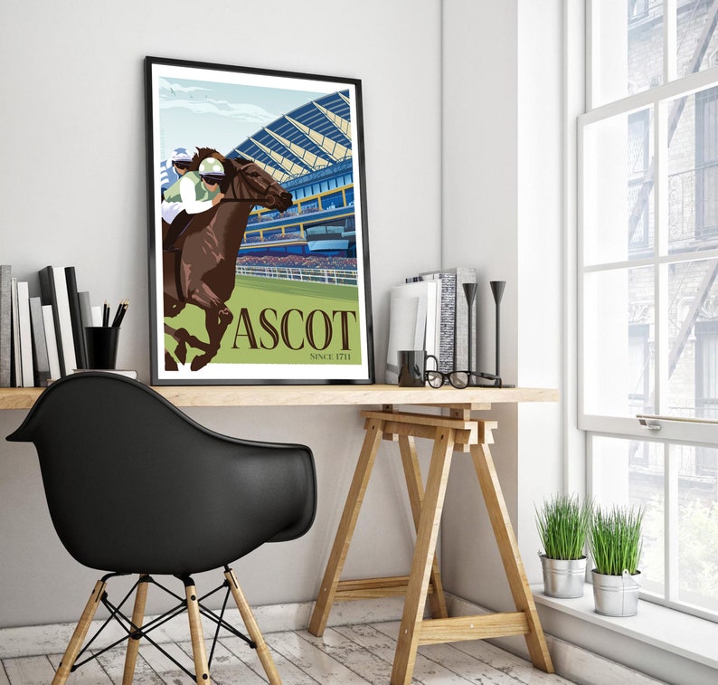 May include: A framed art print featuring a horse race scene at Ascot. The artwork depicts a brown horse with a jockey in green and white racing attire. The word "ASCOT" is displayed in large letters, with "SINCE 1711" below. The print is displayed on a wooden desk.