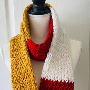 May include: A knitted infinity scarf in red, white, and mustard yellow. The scarf is made with a textured stitch pattern.