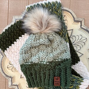 May include: A green and white crocheted hat with a green and white crocheted scarf. The hat has a white pom pom on top and a brown leather tag that says "Ualyou Crafts".