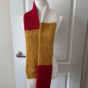 May include: A knitted scarf with red, white, and gold stripes. The scarf is displayed on a white mannequin.