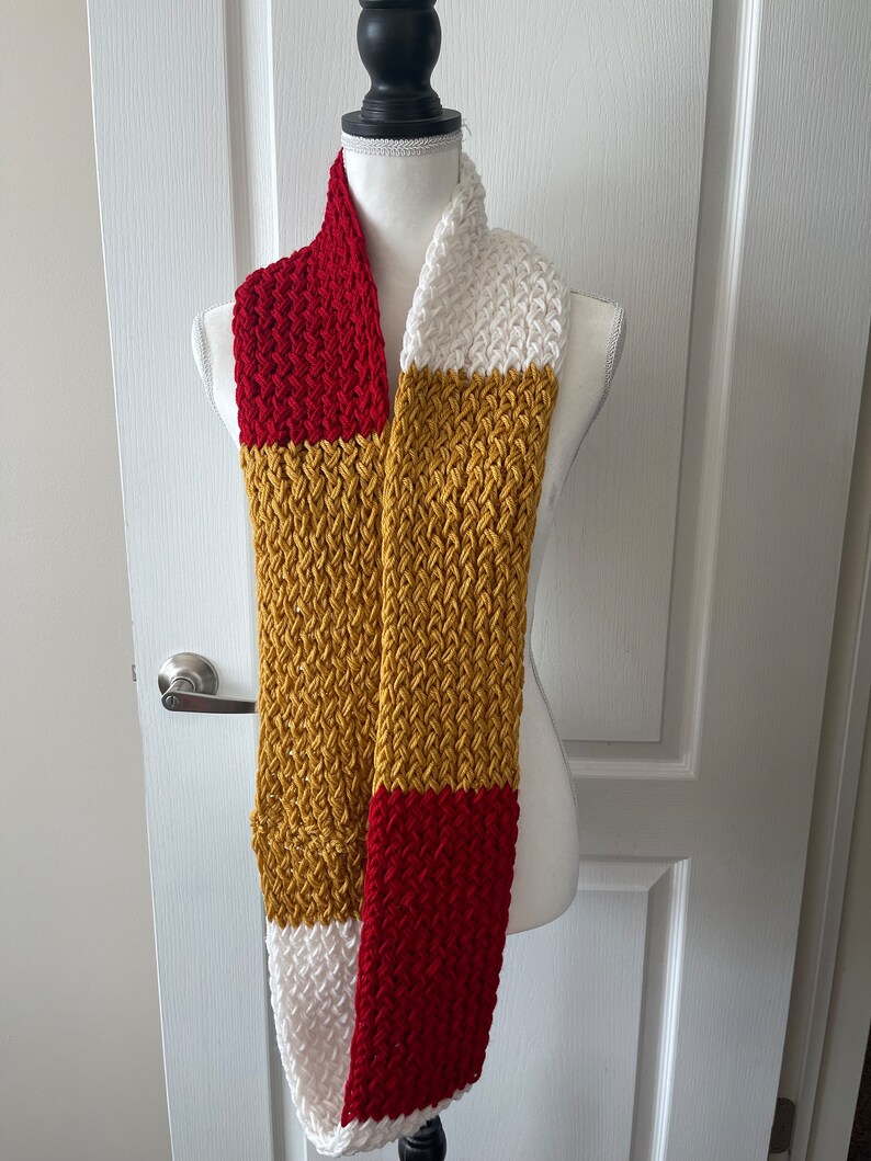 May include: A knitted scarf with red, white, and gold stripes. The scarf is displayed on a white mannequin.