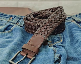 Peut inclure: Une ceinture en cuir tressé marron avec une boucle argentée. La ceinture est posée sur un jean bleu.