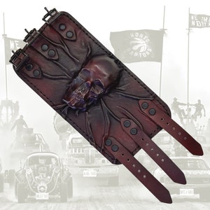 May include: A brown leather wrist cuff with a skull design and multiple straps. The cuff has black metal buckles and rivets. The background is blurred and shows a scene from a film.