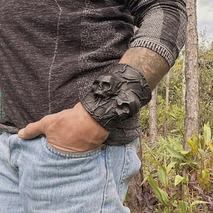Op de afbeelding: Een zwarte leren armband met een schedelontwerp. De armband wordt om de pols gedragen.