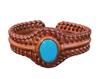 May include: A brown leather bracelet with a woven design and a turquoise stone in the center.
