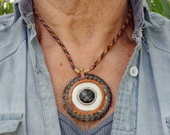 May include: A brown leather necklace with a round pendant. The pendant is made of woven leather and has a silver-colored center with a black stone.