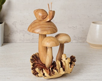 May include: A wooden sculpture of three mushrooms with a snail on top. The mushrooms are brown and have white stems. The snail is brown and has two antennae. The sculpture is sitting on a bed of brown leaves.