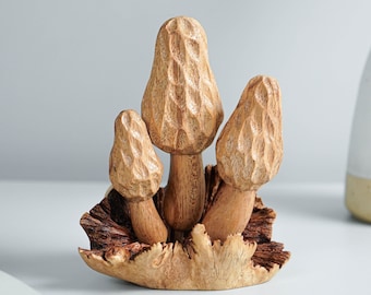 May include: A wooden sculpture of three mushrooms with a brown and black base. The mushrooms are carved with intricate details and have a natural wood finish.