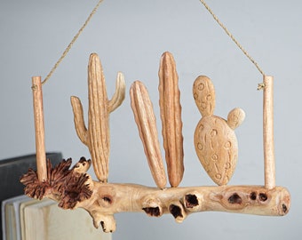 May include: A wooden wall hanging featuring carved cacti and a branch. The cacti are in various shapes and sizes, and the branch is painted brown. The hanging is suspended from a string.