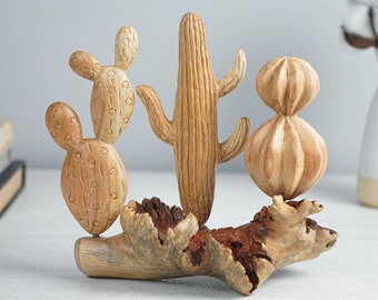 Puede incluir: Una escultura decorativa que presenta tres figuras de cactus de color marrón claro montadas sobre una pieza de madera flotante texturizada de color marrón oscuro. Los cactus muestran formas variadas, incluyendo un estilo nopal.