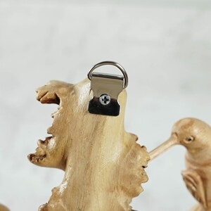 May include: Wooden wall decor featuring two carved hummingbirds perched on a branch. The piece has a metal hanging hook on the back.