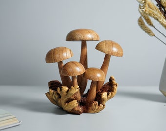 Può includere: Una scultura decorativa composta da cinque funghi in legno marrone chiaro, lisci e di altezze variabili. I cappelli sono arrotondati e levigati, fissati su steli sottili ancorati a una base in legno naturale dalla consistenza nodosa.