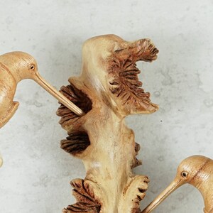 May include: A wooden sculpture of three hummingbirds perched on a branch. The birds are carved in detail and have realistic features. The branch is also carved with intricate details.