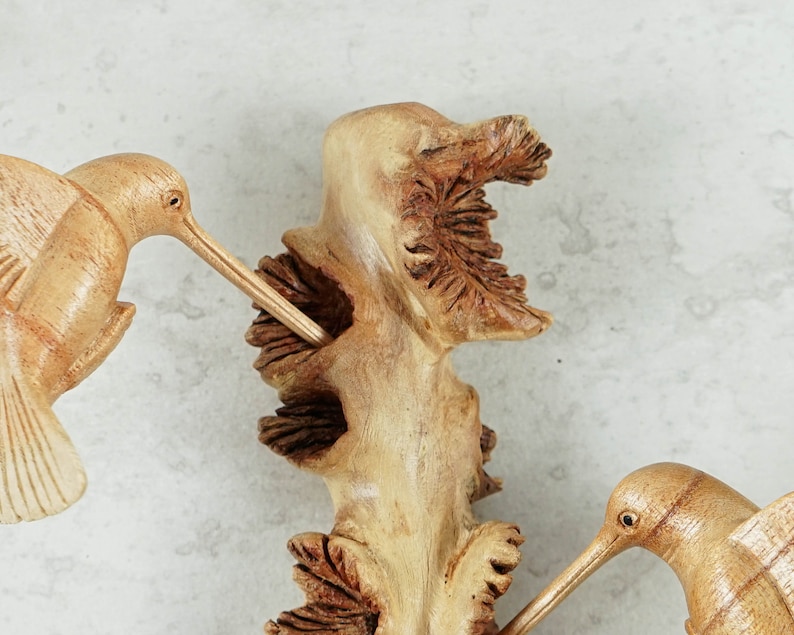 May include: A wooden sculpture of three hummingbirds perched on a branch. The birds are carved in detail and have realistic features. The branch is also carved with intricate details.