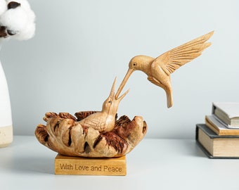 May include: A wooden sculpture of two hummingbirds, one feeding the other. The sculpture is on a wooden base with the words "With Love and Peace" engraved on it.