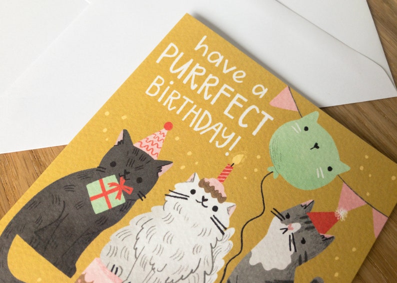 May include: A yellow birthday card with the text "have a purrfect birthday!" and three cats wearing party hats. One cat is holding a gift, another is wearing a cake hat with a candle, and the third is holding a green balloon.
