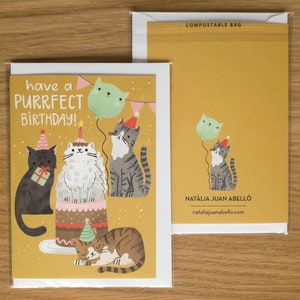May include: A yellow birthday card with a cat theme. The card features five cats, a birthday cake, and balloons. The text on the card reads "have a purrfect birthday!"