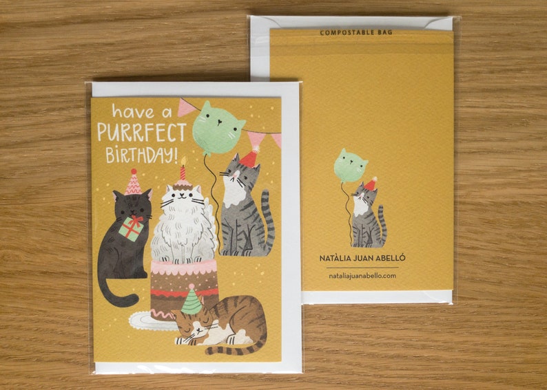 May include: A yellow birthday card with a cat theme. The card features five cats, a birthday cake, and balloons. The text on the card reads "have a purrfect birthday!"