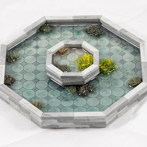 Peut inclure: Une fontaine octogonale miniature avec une fontaine octogonale plus petite au centre. Les deux fontaines sont en pierre grise et ont une base carrelée verte. Les fontaines sont entourées de petites plantes vertes.