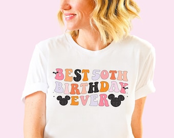 May include: White t-shirt with a colorful graphic that says "BEST 50TH BIRTHDAY EVER" with Mickey Mouse ears on either side of the text.