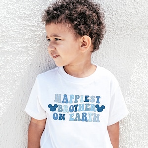 May include: A white t-shirt with a blue and white graphic that says "Happiest Brother on Earth" with Mickey Mouse ears on either side of the text.