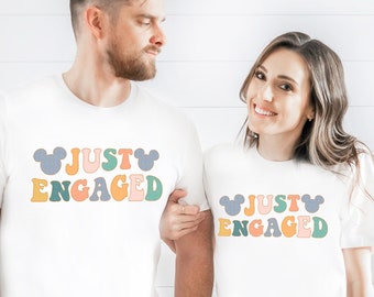 May include: Two white t-shirts with the text "Just Engaged" in colourful letters and Mickey Mouse ears on either side.