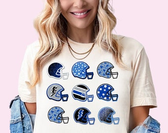 May include: A white t-shirt with a design of nine blue and white football helmets. Each helmet has a different pattern, including stars, lightning bolts, and camouflage.