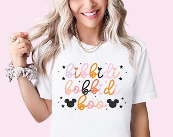 May include: White t-shirt with a graphic design that says "Bibbidi Bobbidi Boo" in colorful script with black Mickey Mouse ears on either side of the text.