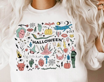 May include: White sweatshirt with a colorful Halloween-themed graphic print featuring a variety of spooky and whimsical illustrations, including a witch, a cat, a pumpkin, and the words "Halloween" and "Witchcraft".