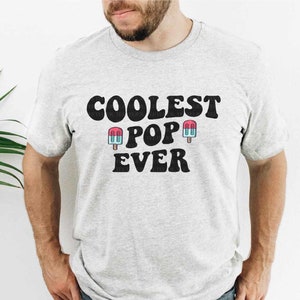 May include: A gray t-shirt with the text "Coolest Pop Ever" in black with two blue and pink popsicle graphics.