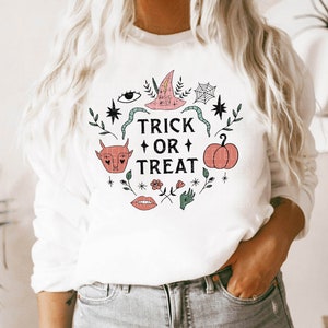 May include: White sweatshirt with a graphic design of a pumpkin, a witch's hat, and other Halloween-themed elements. The text "Trick or Treat" is printed in black.