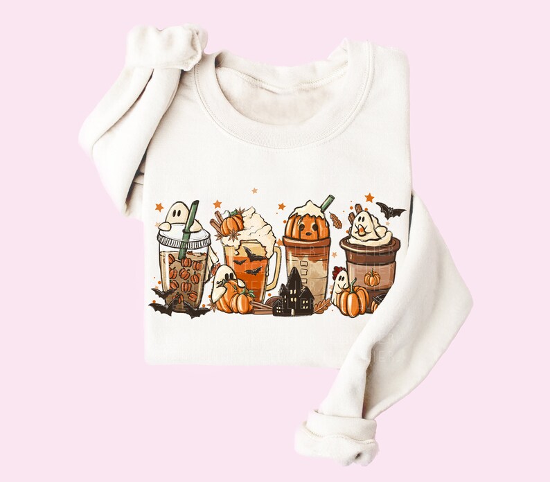 May include: A white sweatshirt with a graphic print of four pumpkin spice-themed drinks with ghosts, bats, and stars. The drinks are decorated with whipped cream, sprinkles, and pumpkin accents.