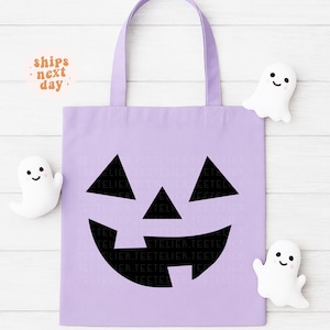 May include: A light purple tote bag with a black jack-o'-lantern face design. The bag has a matching handle and is decorated with three white ghost-shaped plushies. The text "ships next day" is in the upper left corner.