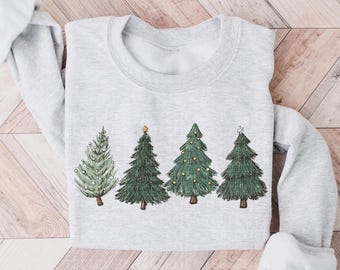 Puede incluir: Una sudadera de cuello redondo en color gris claro con un estampado gráfico de cuatro árboles de hoja perenne estilizados. Los árboles están representados en varios tonos de verde con detalles dibujados a mano, incluyendo adornos amarillos y una estrella.
