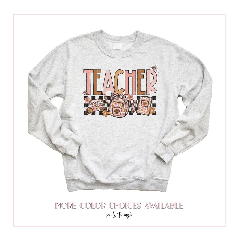 Puede incluir: Una sudadera gris con la palabra "TEACHER" impresa en letras rosas y marrones. El dise&ntilde;o incluye un patr&oacute;n a cuadros, un autob&uacute;s escolar, una mochila y un libro.