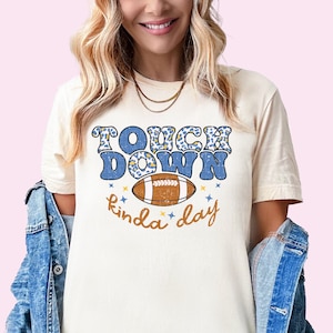 May include: A cream coloured t-shirt with a blue and yellow graphic that says "Touch Down kinda day" with a football in the middle.