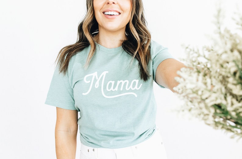 Puede incluir: Una camiseta azul claro con la palabra "Mama" escrita en cursiva blanca.