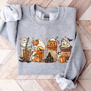 May include: A gray sweatshirt with a graphic print of fall-themed drinks with ghosts and pumpkins. The drinks are iced coffee, pumpkin spice latte, and a hot chocolate.