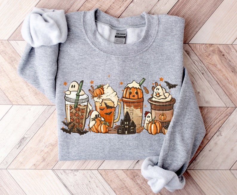 May include: A gray sweatshirt with a graphic print of fall-themed drinks with ghosts and pumpkins. The drinks are iced coffee, pumpkin spice latte, and a hot chocolate.