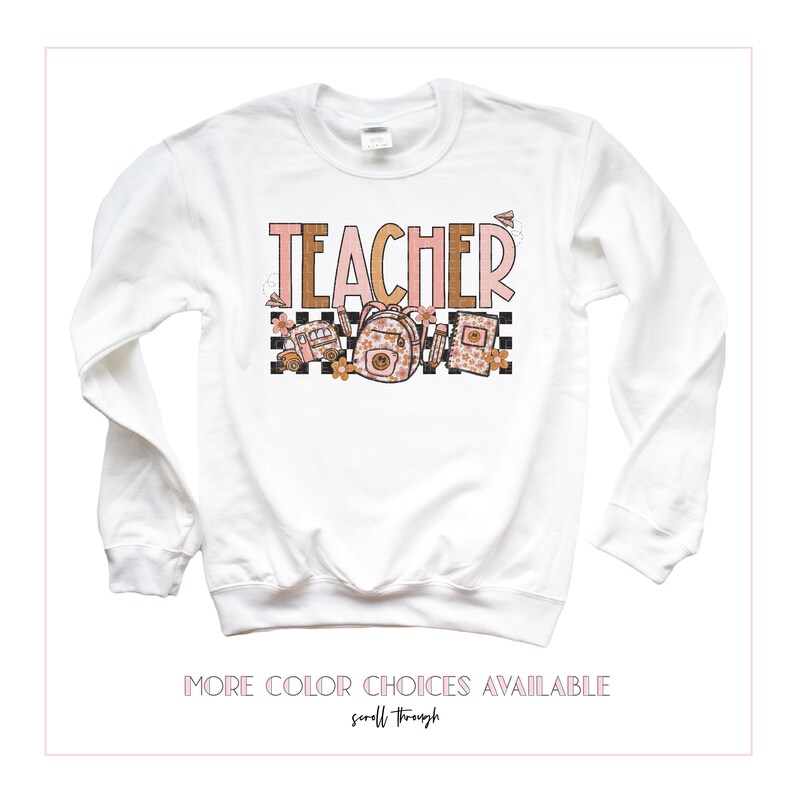 Puede incluir: Sudadera blanca de manga larga con la palabra "TEACHER" en letras rosas y marrones. El dise&ntilde;o incluye un patr&oacute;n a cuadros, un autob&uacute;s escolar, una mochila y l&aacute;pices. El texto "MORE COLOR CHOICES AVAILABLE" est&aacute; en la parte inferior de la imagen.
