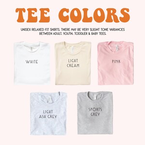 May include: Image of five folded unisex relaxed fit t-shirts in various colors: white, light cream, pink, light ash grey, and sports grey. The shirts have text labels indicating the color. The text "TEE COLORS" is at the top.