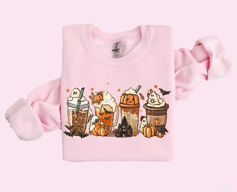 May include: A pink sweatshirt with a graphic of five fall-themed coffee drinks with ghosts, pumpkins, and bats. The drinks are topped with whipped cream, pumpkin spice, and sprinkles.