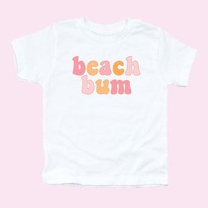 May include: White t-shirt with the text "beach bum" in pink, orange and yellow retro-style lettering.