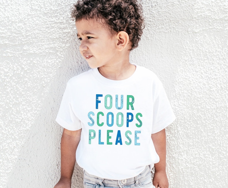 May include: A white t-shirt with the text "FOUR SCOOPS PLEASE" in blue and green lettering. The shirt is worn by a young child. The text has a watercolor effect.