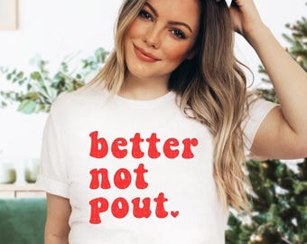 May include: White t-shirt with the red text "better not pout." The shirt has short sleeves and a crew neck. The text is in a bold, playful font. The shirt is worn by a person with long, wavy blonde hair.