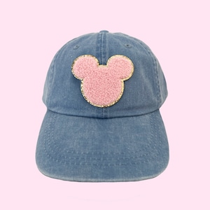 May include: A blue denim baseball cap with a pink and gold Mickey Mouse head patch.