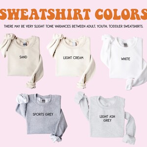 Puede incluir: Cinco sudaderas de diferentes colores dispuestas sobre un fondo rosa. Los colores son arena, crema claro, blanco, gris deportivo y gris ceniza claro. El texto "SWEATSHIRT COLORS" est&aacute; en la parte superior de la imagen. El texto "THERE MAY BE VERY SLIGHT TONE VARIANCES BETWEEN ADULT, YOUTH, TODDLER SWEATSHIRTS." est&aacute; debajo del t&iacute;tulo.