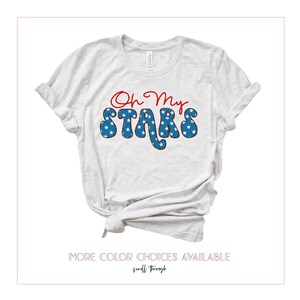 May include: A light gray t-shirt with the text "Oh My Stars" in red and blue. The text is in a retro font and features a pattern of white stars on a blue background.